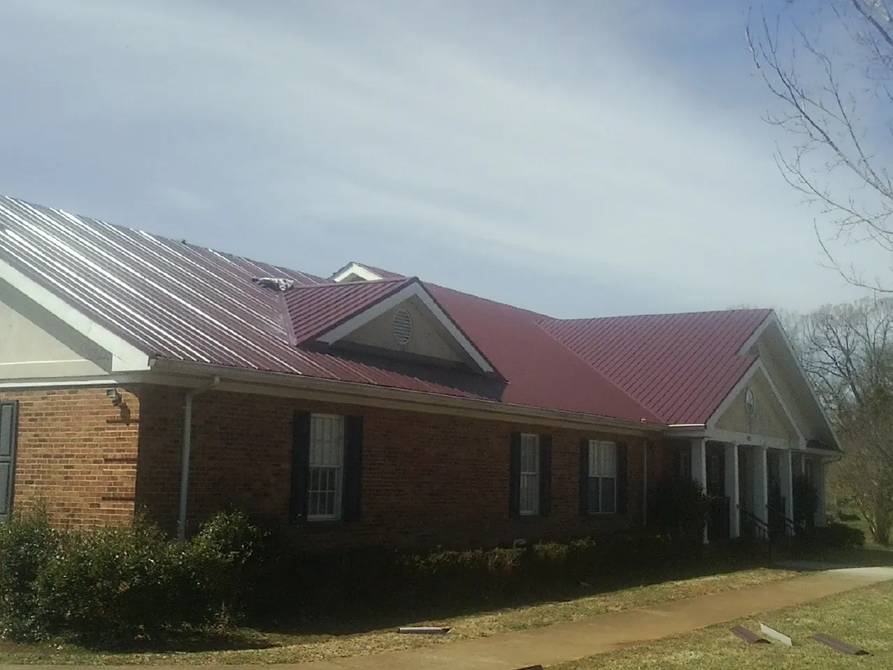 Red metal roof with gabled entries on a long brick building, from a Hail Damage Roof Repair job in Andalusia