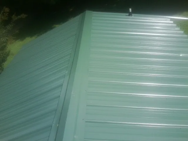 New green metal panels meeting at the ridge of a roof — Flat Roof Repair work by our crew in Andalusia