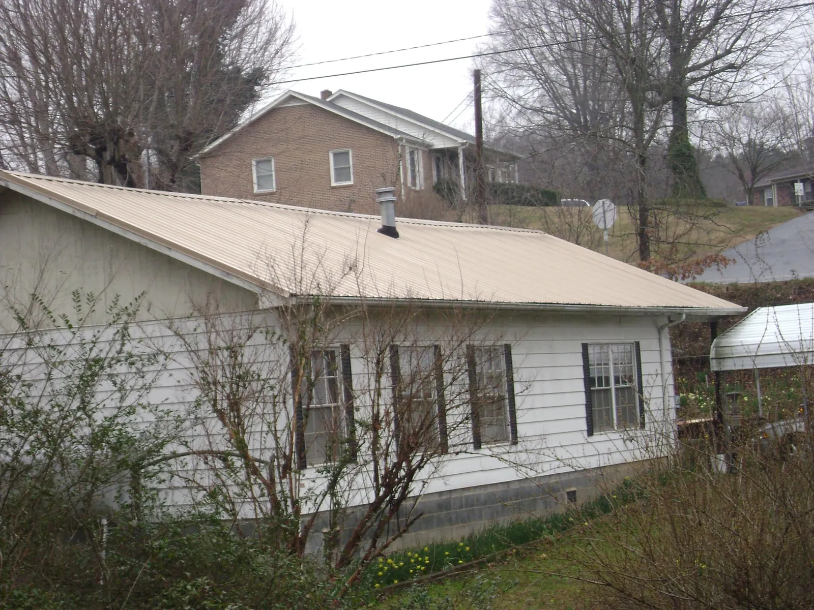 Tan metal roof on a white sided house set into a hillside — Commercial Roofing by Roofing Brothers in Andalusia